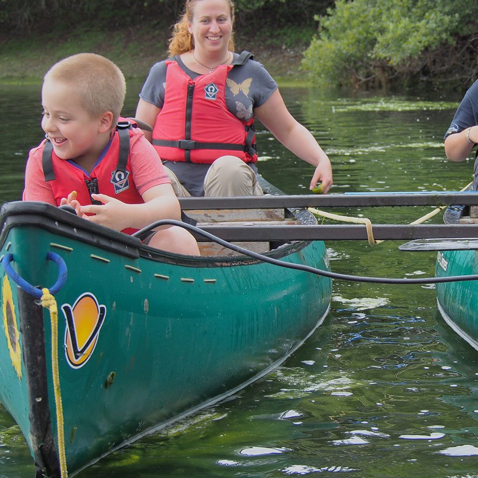 Smiling woman and boy wearing life jackets, sitting in a canoe on the water