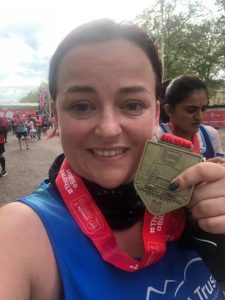 Lady holding a London Marathon medal to her face, smiling at the camera