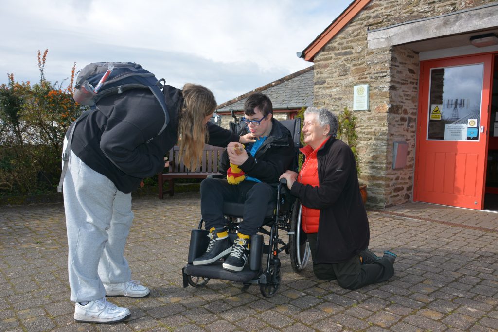 A lady touching the face of a man in a wheelchair with another lady kneeling down beside him