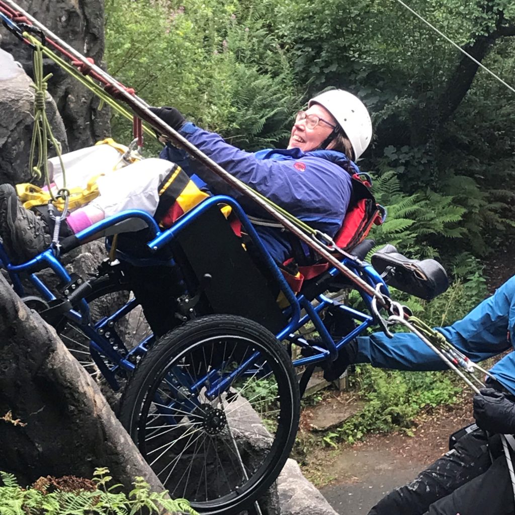 A lady in a wheelchair going down an outdoor climbing wall