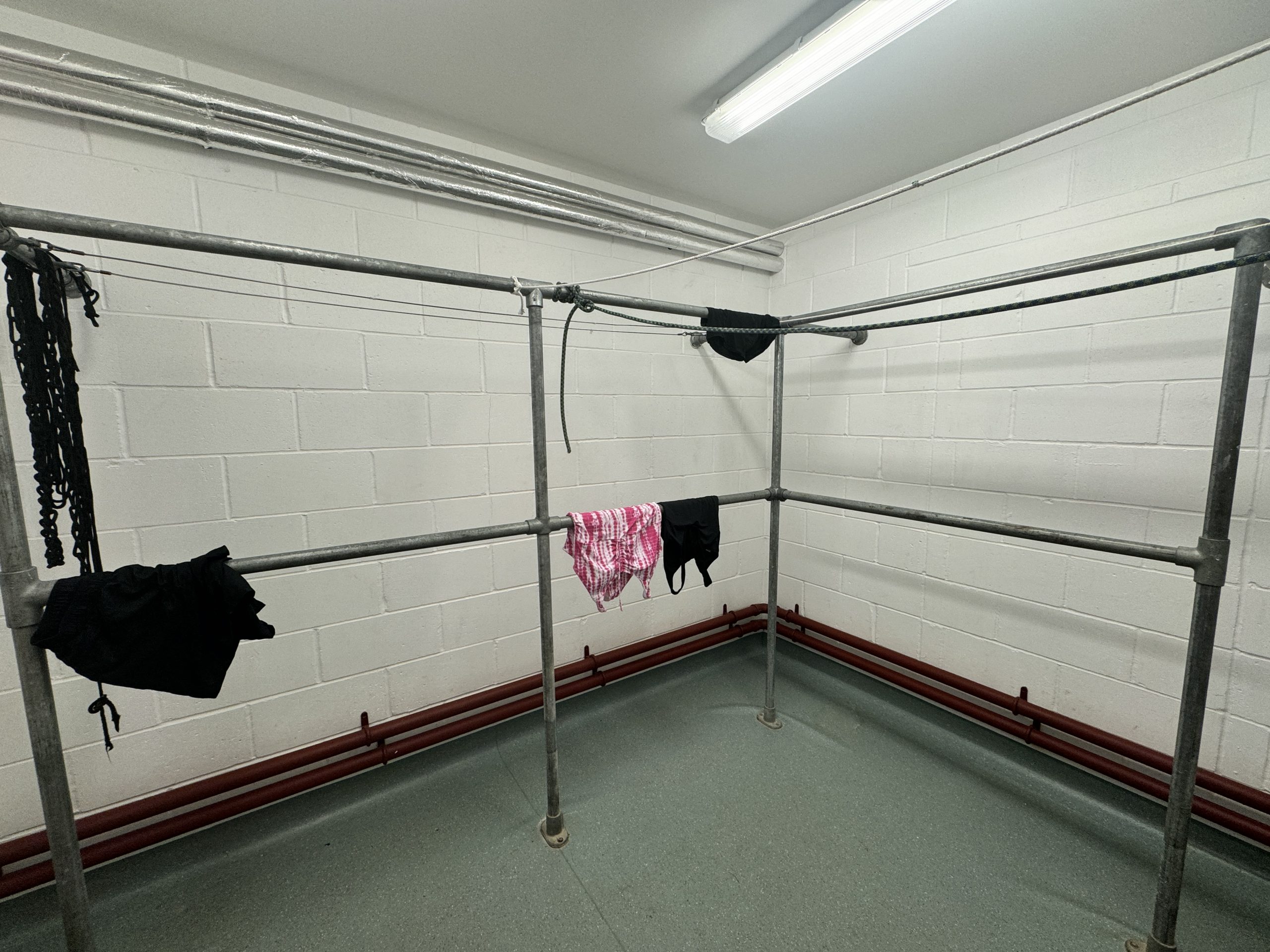 A room with metal bar frames with a few items of clothing dangled over them to dry