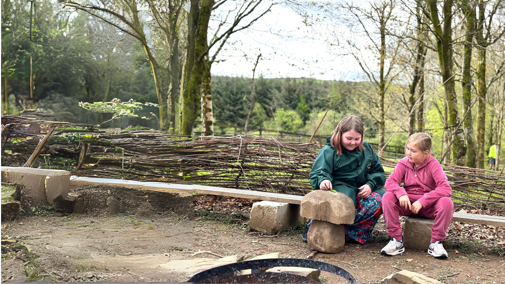 Two young girls are sitting on a bench in the outdoors, with woven planted fencing behind and under trees in a woodland. They are looking at a leaf together and smiling.