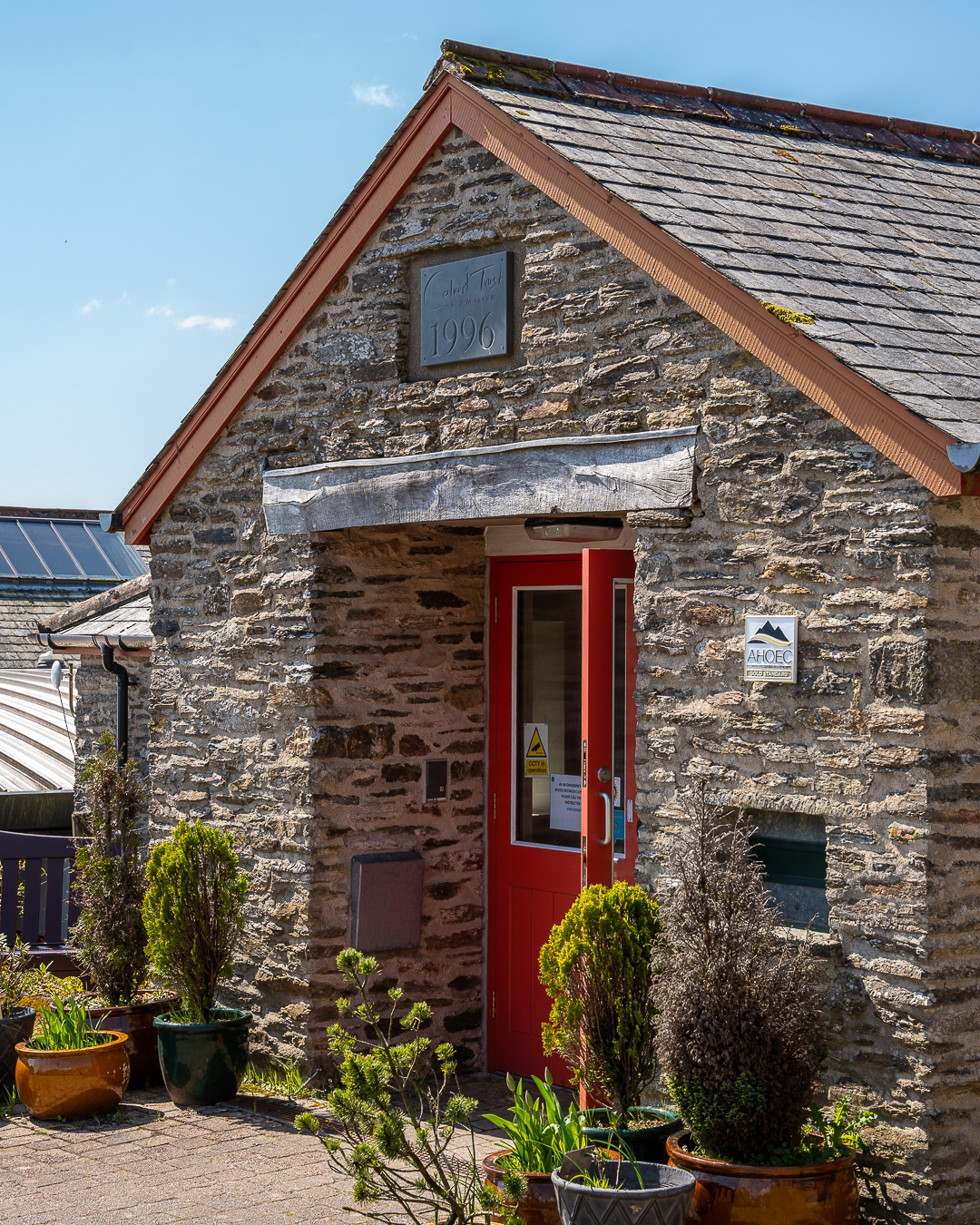 A photograph of the entrance to Calvert Exmoor's Reception building. The door is a bright red, with a slate sign above it reading 