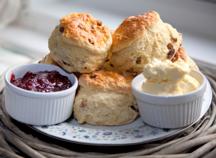 Three scones on a plate with a dish of jam on the left side and a dish of cream on the other side of the plate.