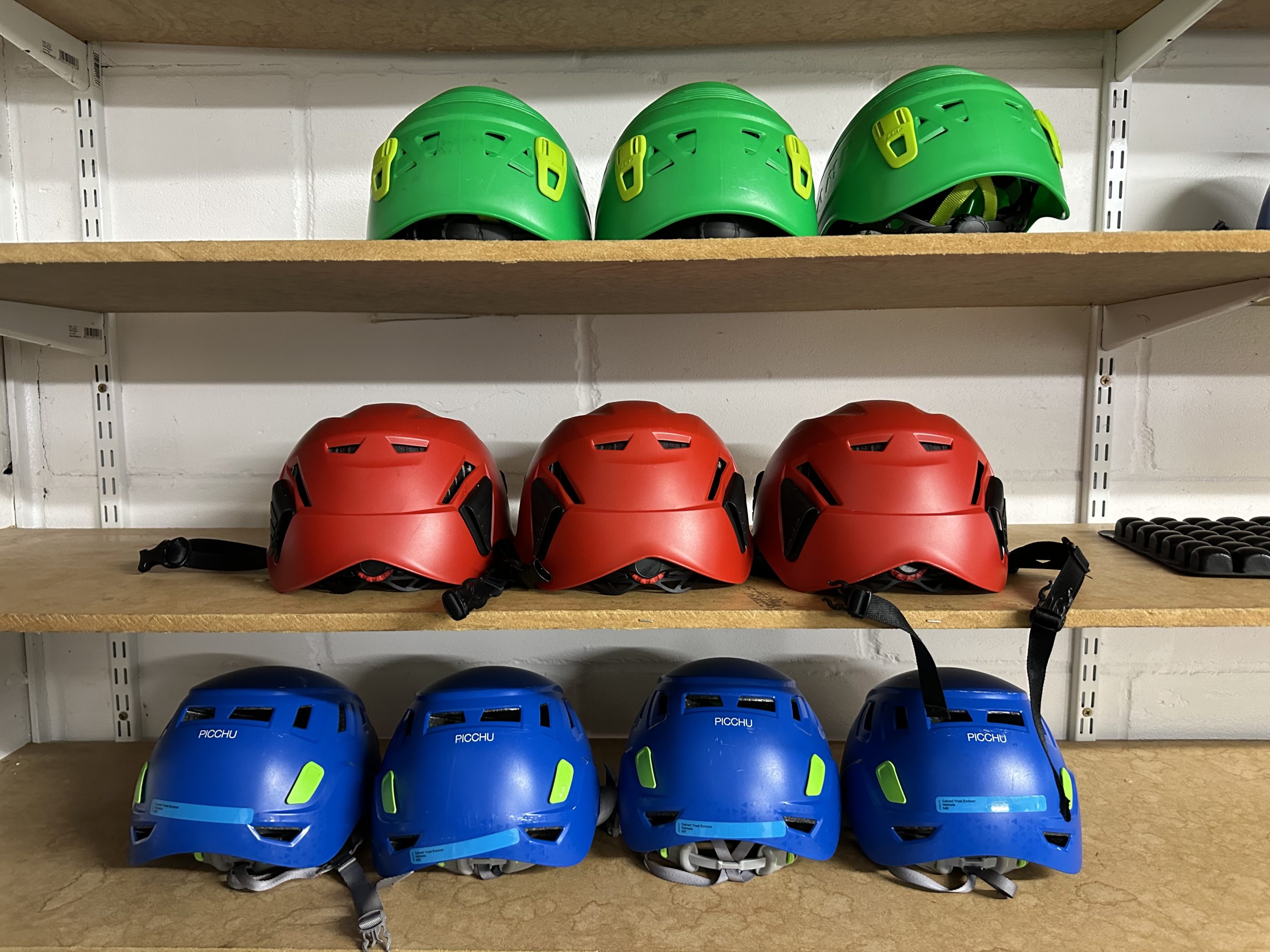 Three shelves with three green helmets on the top shelf, three red helmets on the central shelf and four blue helmets on the bottom shelf.