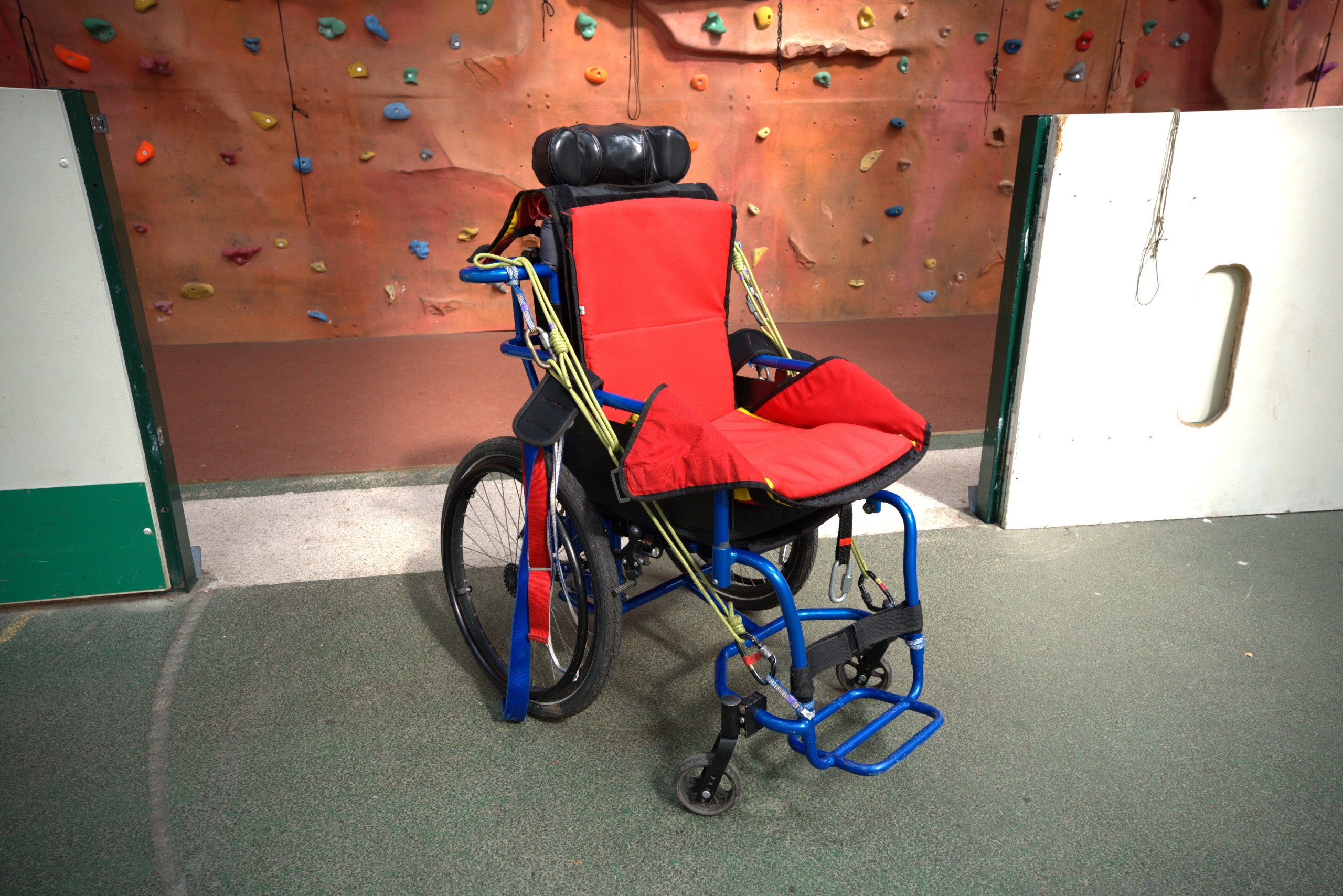 The blue Abseiling wheelchair with a red seat shaped cushion inside in the middle of the floor to showcase the equipment.