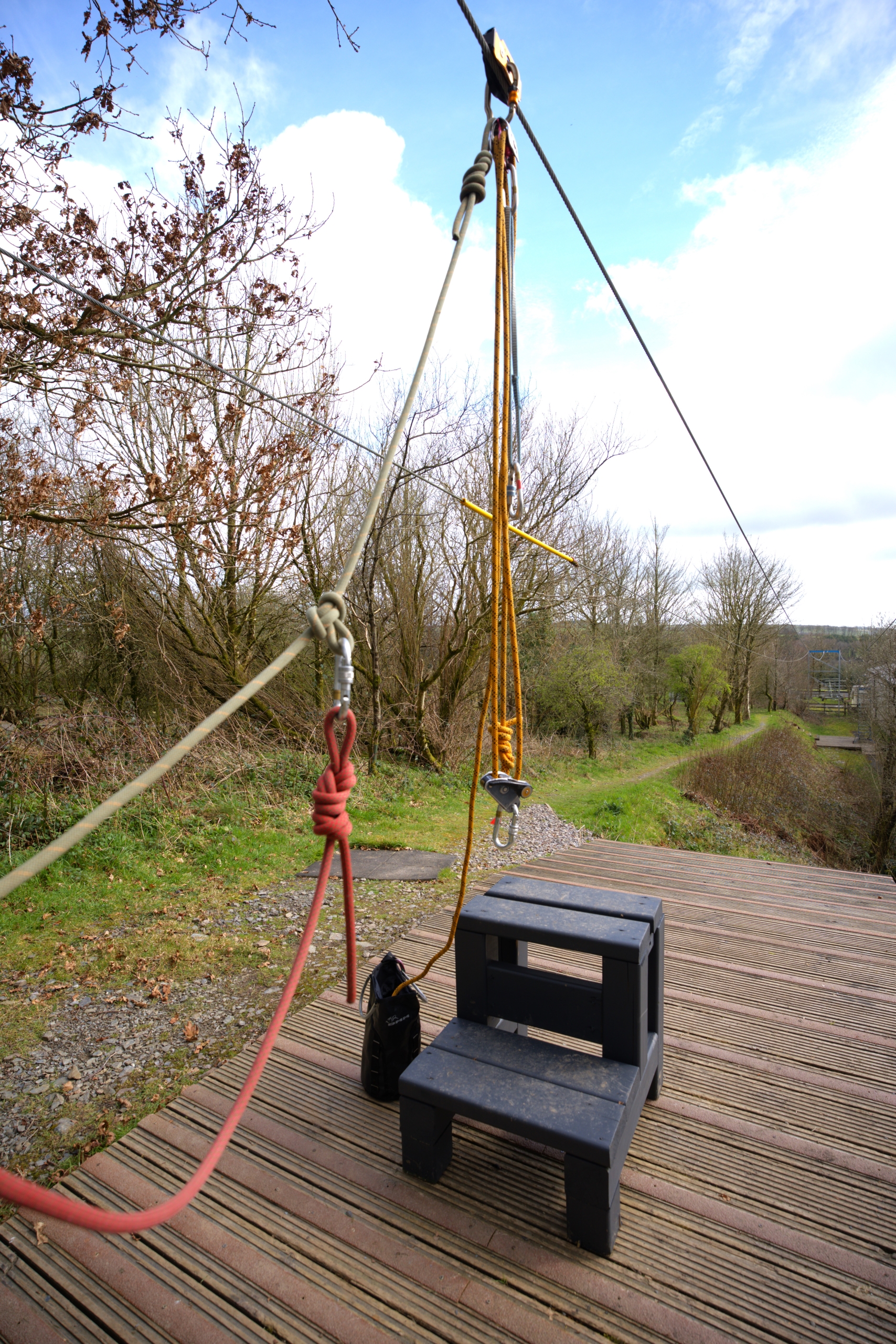 An empty set up for Zipwire activity, including some black steps for guests to climb higher and be attached to the yellow hanging rope and red safety rope.