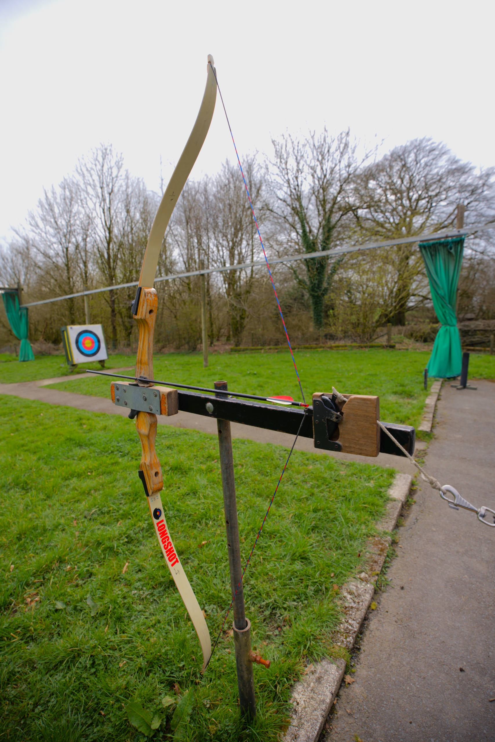 An accessible trigger bow is loaded and ready to fire, positioned on top of a pole to keep it steady and facing left to shoot a target.