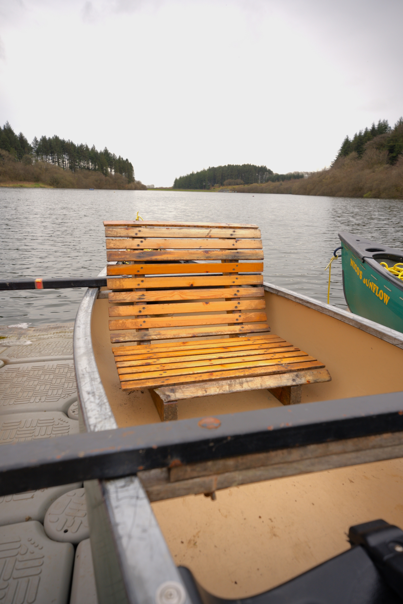 A wooden slatted seat inside a canoe on a jetty with the reservoir behind.
