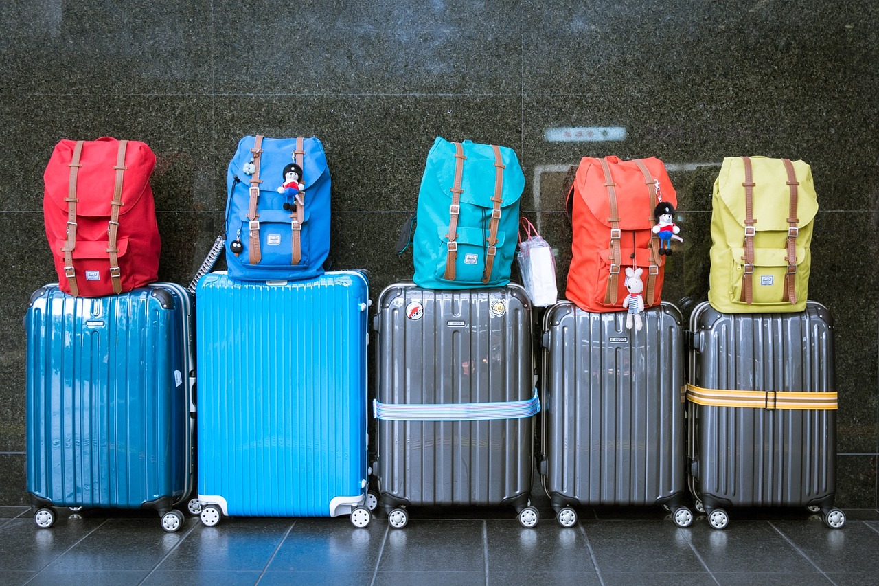 A row of suitcases with a backpack on each one stand in front of a black tiled wall.