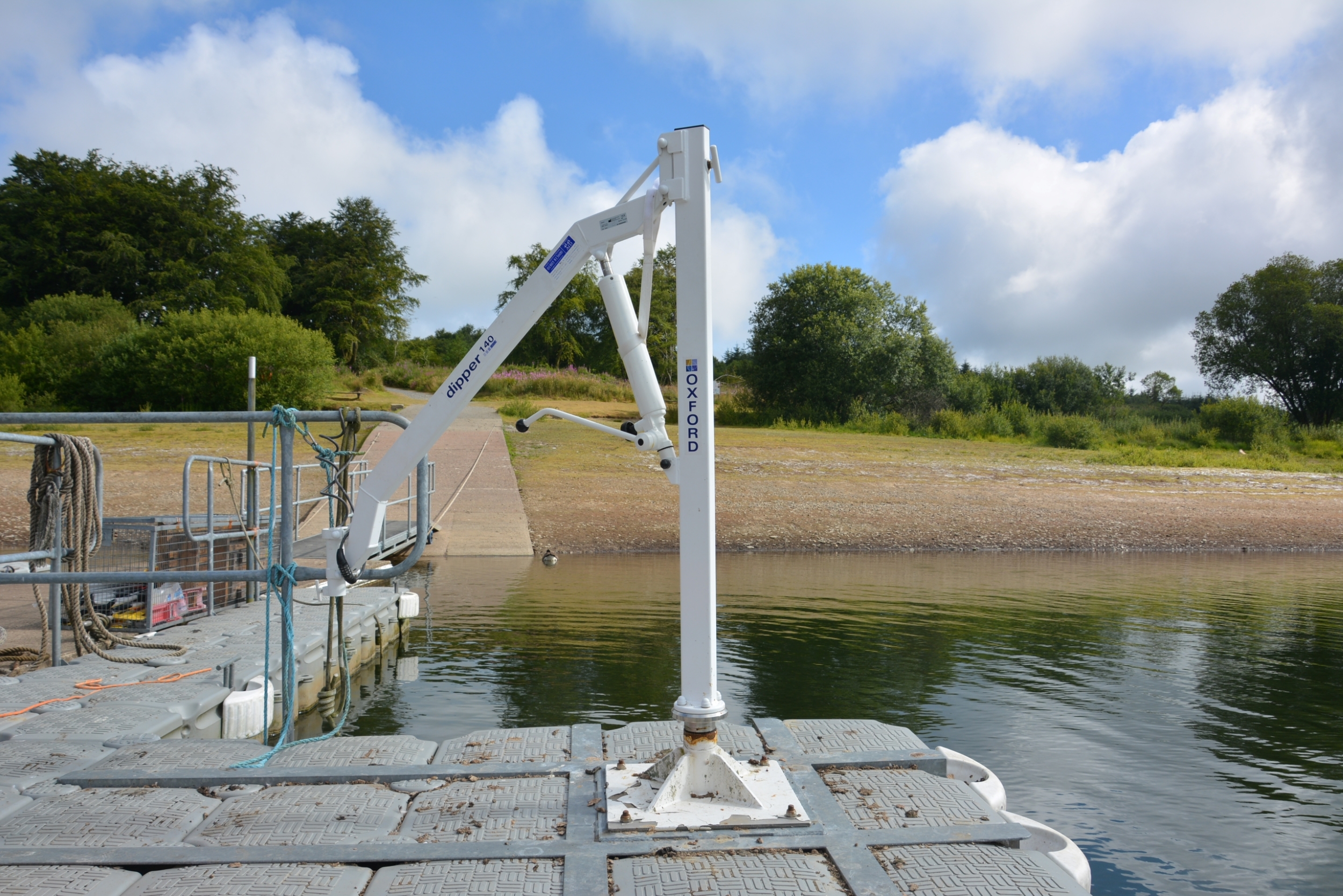 A white mechanic machine standing upright from a jetty surrounded by water.