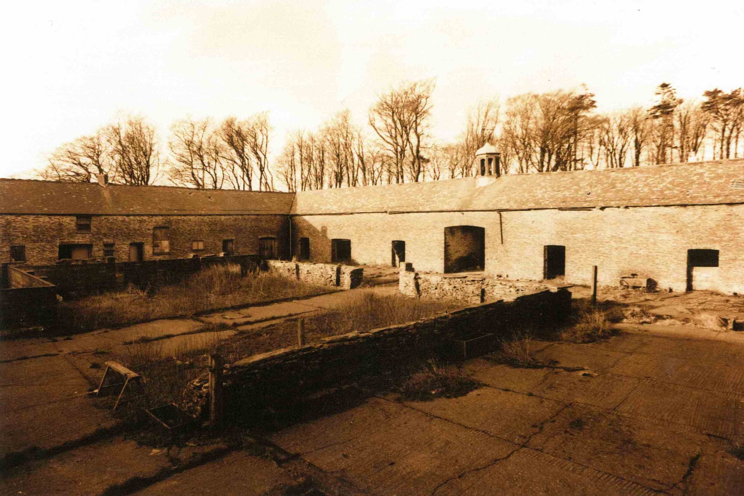 A sepia image of a messy stone-built courtyard of farm buildings